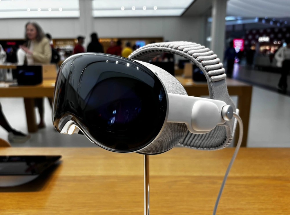 An Apple Vision Pro headset on display in an Apple Store, with shoppers browsing in the background