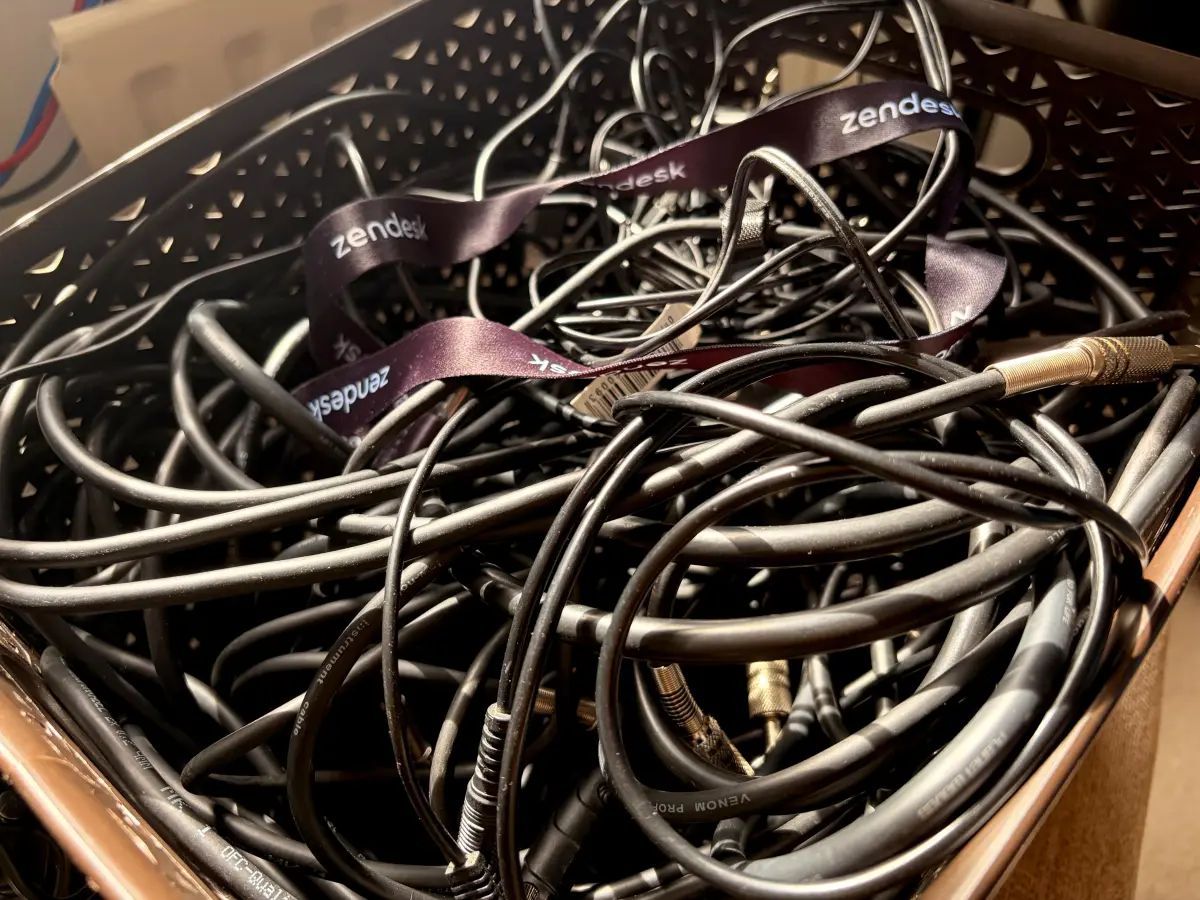 A cardboard box full of tangled black cables, with Zendesk-branded lanyards draped on top